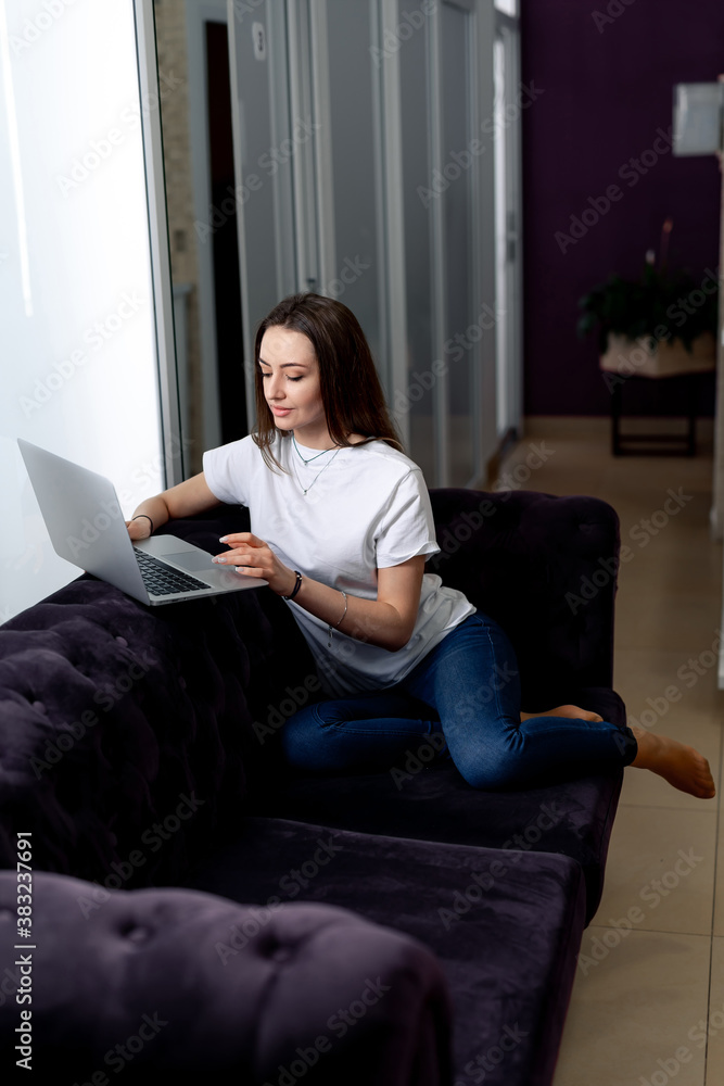 Smiling happy woman sitting on the sofa and using laptop. Woman working at home.