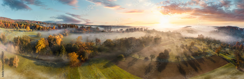 Stunning aerial panorama of a misty rural landscape at sunrise, with colorful autumn trees, fields a