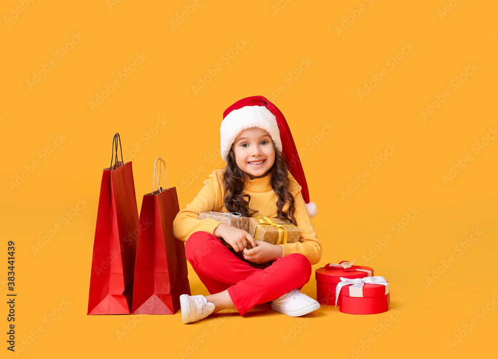 Cute little girl in Santa hat, with gift boxes and shopping bags on color background