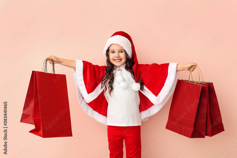 Cute little girl in Santa costume and with shopping bags on color background