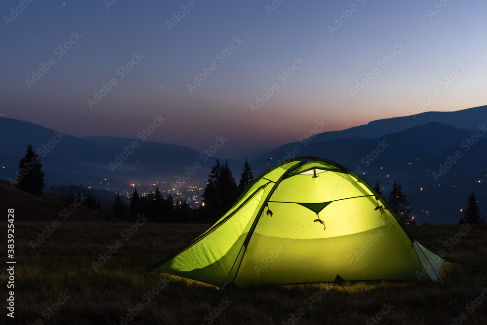在令人难以置信的山脉背景下，用手电筒从内部照亮绿色帐篷
