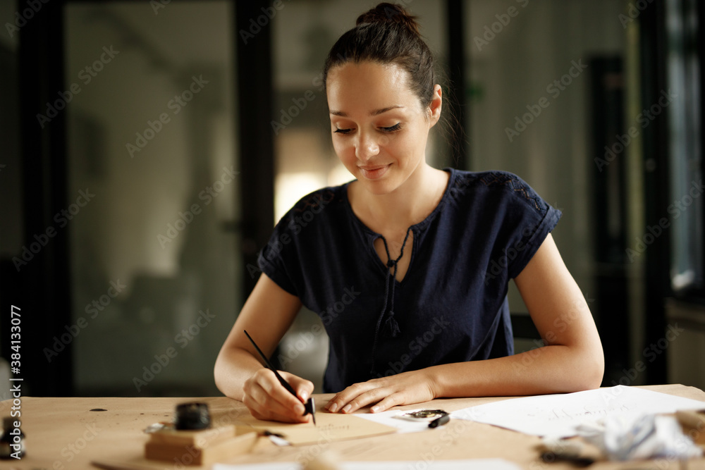 美丽微笑的年轻女子用自来水笔写字。书法家在工作。
