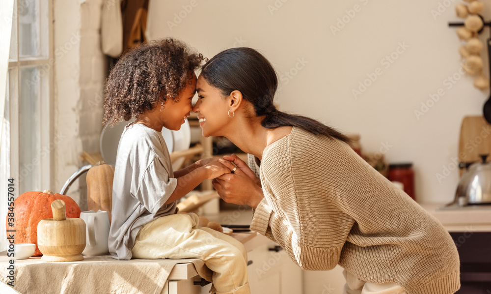 Happy ethnic family mother and   son kiss and laugh in the kitchen at home.