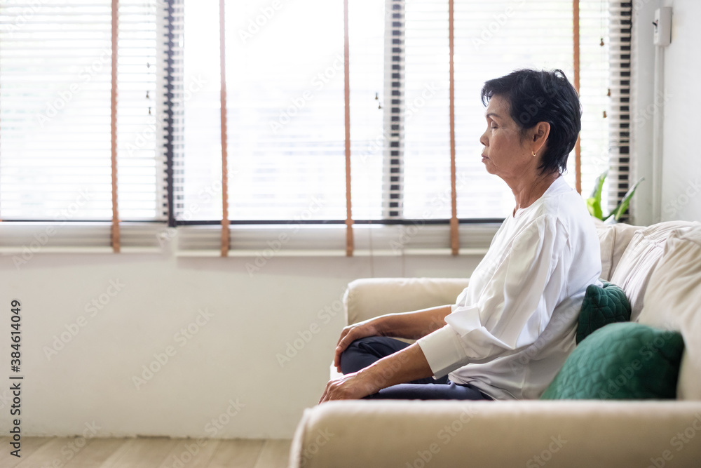 亚洲老年妇女坐在沙发上，在家练习瑜伽和冥想，退休和幸福