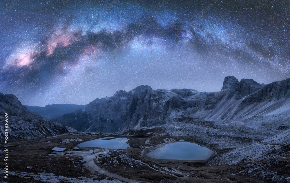 Milky Way arch over mountains at night in summer. Landscape with alpine mountains, lake, purple sky 
