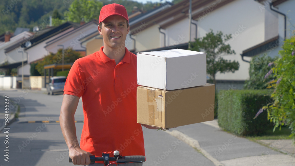 CLOSE UP: Parcel delivery man holds two boxes in one hand while riding escooter.