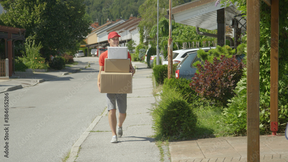 Young male courier leisurely strolls along the sidewalk carrying big packages.