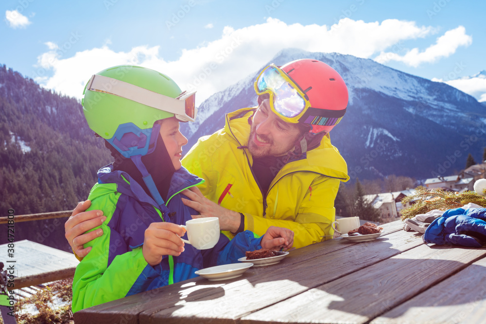 父亲搂着肩膀，穿着滑雪服的小男孩在s后享受山景午休