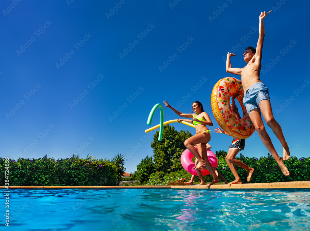 Many of happy teenage kids dive in the swimming pool water throw inflatable toys lifting hands have 