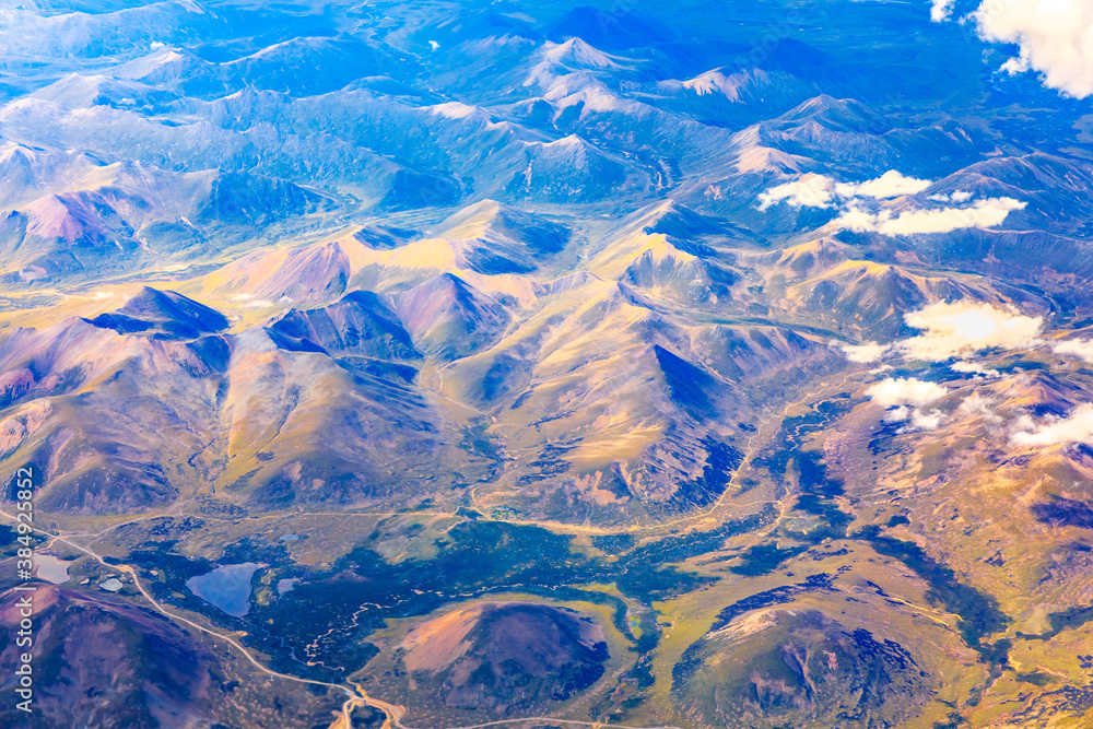 在阳光明媚的日子里俯瞰云朵和五颜六色的山脉。从飞机上俯瞰山脉。