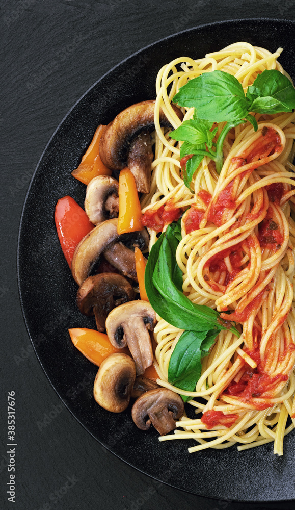 意大利面配蘑菇和蔬菜，放在黑色盘子里。菜单概念。俯视图。