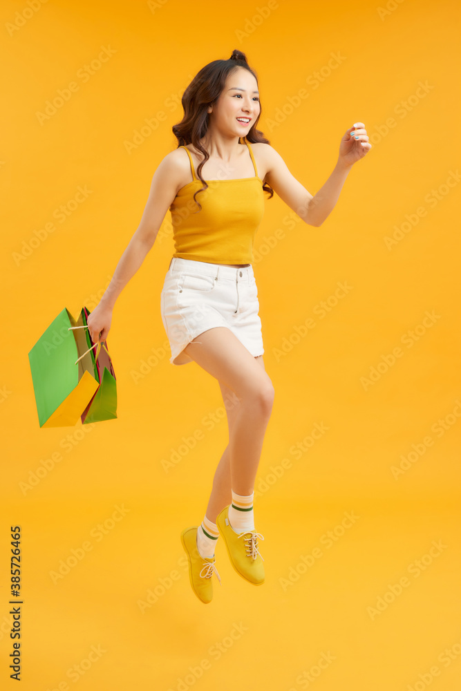 attractive happy woman jumping running holding shopping bags over orange background. Summer concept