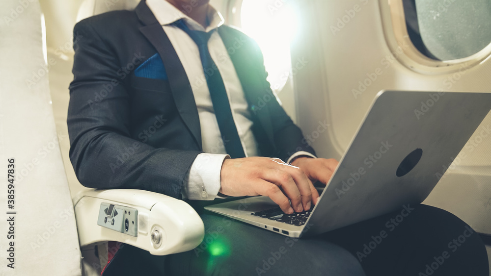 Young businessman using laptop computer in airplane . Business trip travel concept .