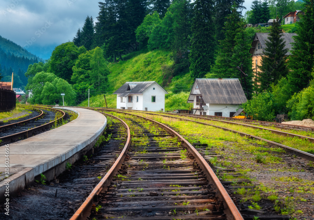 Railway station and small white house in mountain village at sunset. Rural railroad in overcast day 