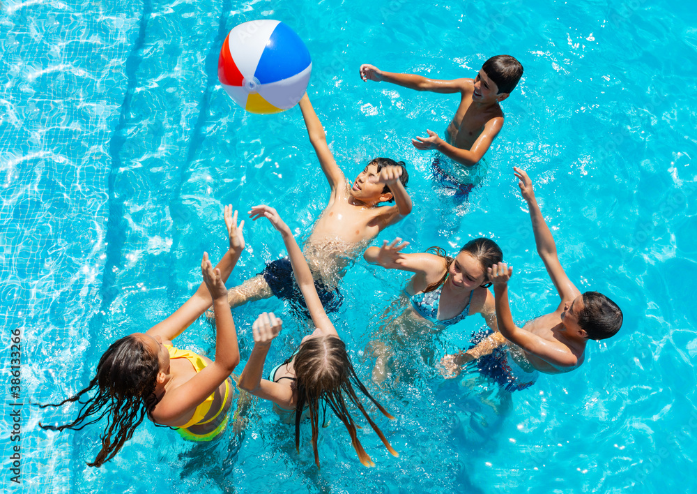 一群孩子追着球跳，在游泳池里玩，溅水，举起手微笑