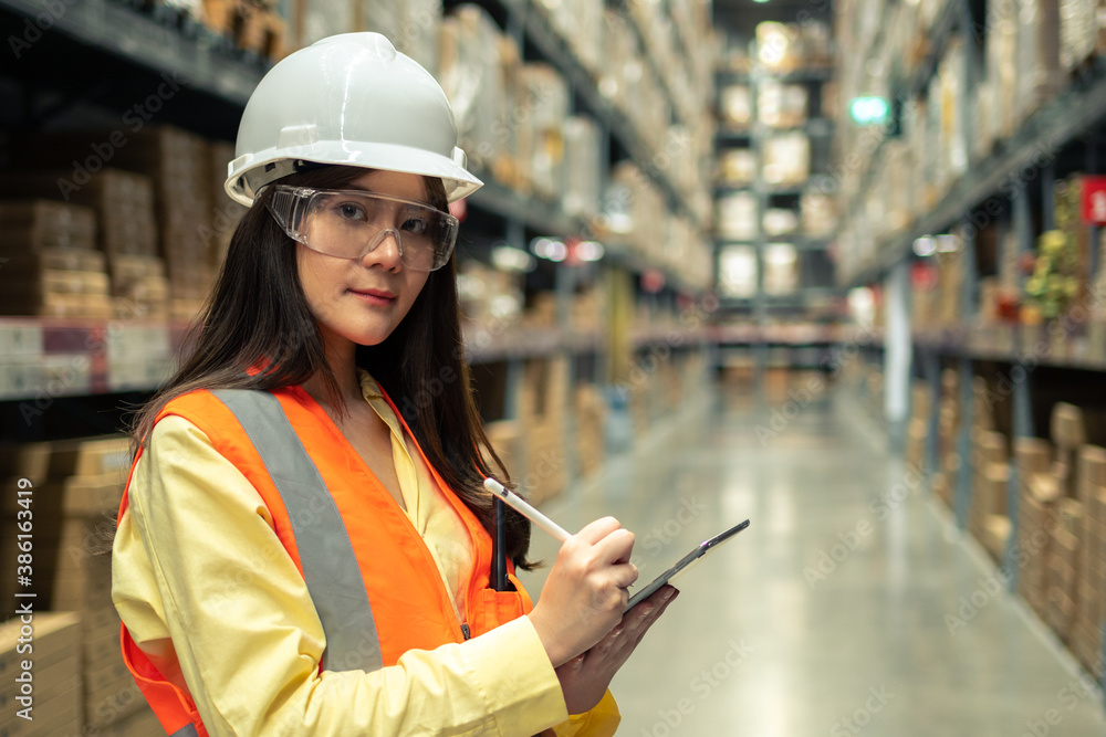 Female warehouse worker inspecting a warehouse in a factory. Wear a safety helmet and glasses for wo