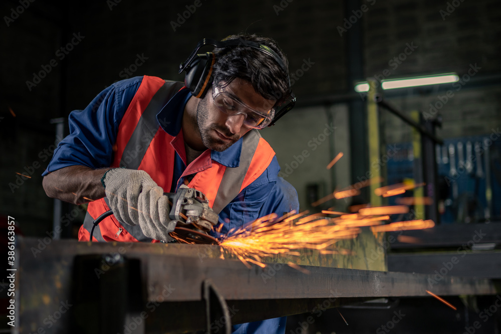 一名男性工程师正在一家工业工厂里打磨钢材。