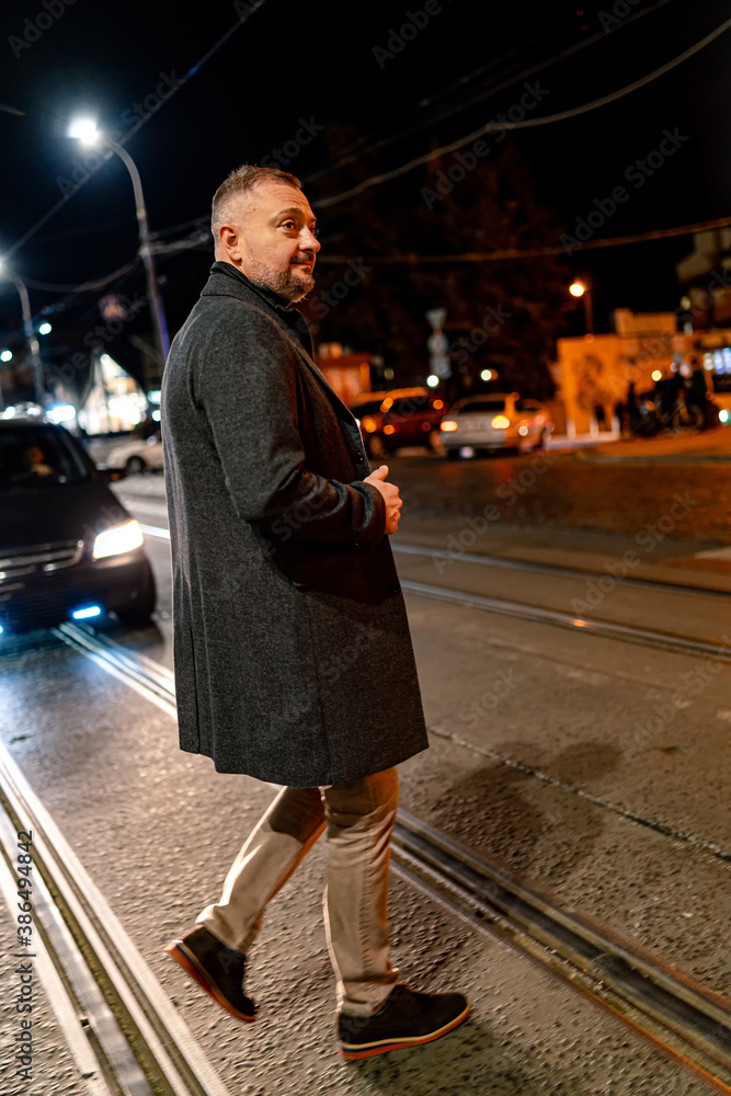 穿着深灰色外套的时尚男子走在街上。晚上拍照。成熟优雅的bu