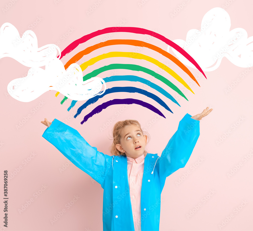 Cute little girl in raincoat on color background with drawn rainbow and clouds