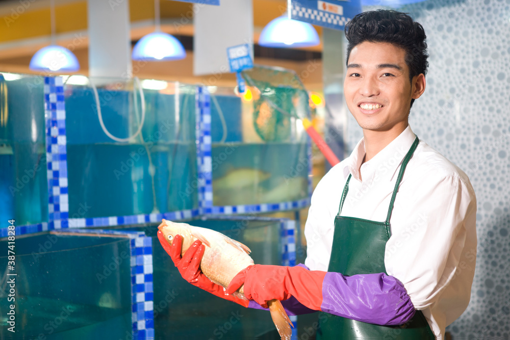 一位超市海鲜销售员拿着鱼的优质照片