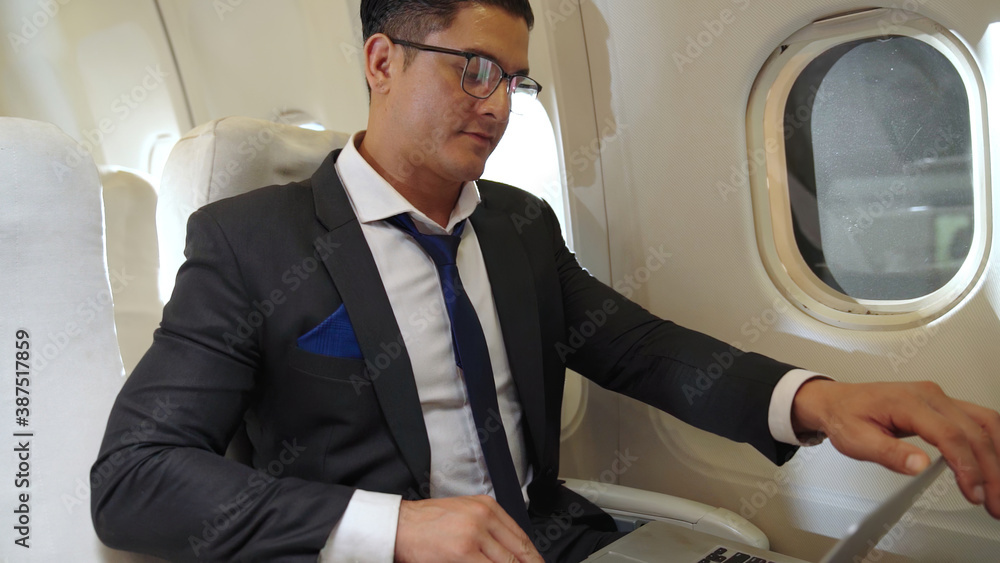 Young businessman using laptop computer in airplane . Business trip travel concept .