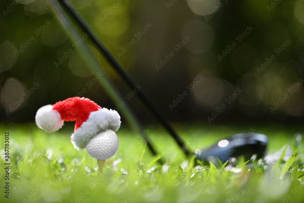 Festive-looking golf ball on tee with Santa Claus hat on top for holiday season on golf course back