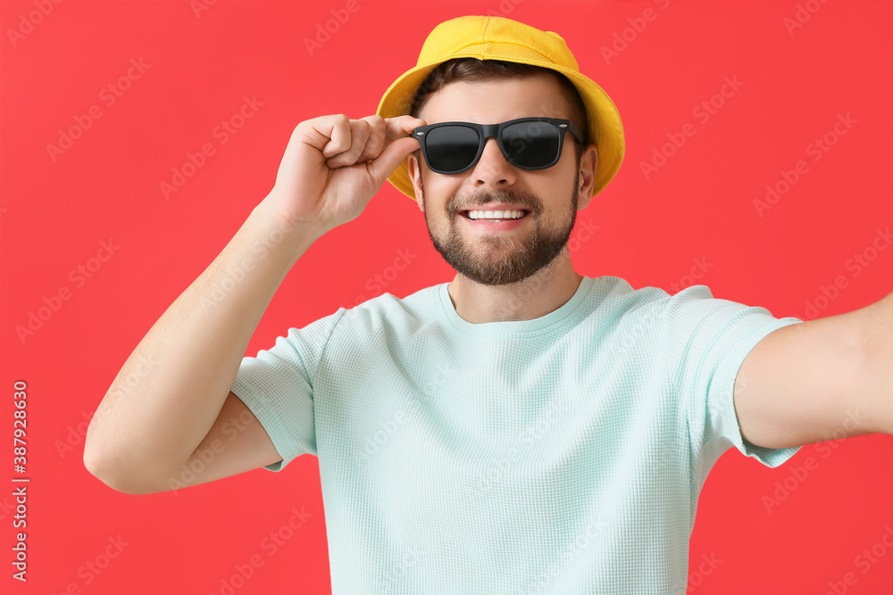 Handsome man with stylish sunglasses taking selfie on color background