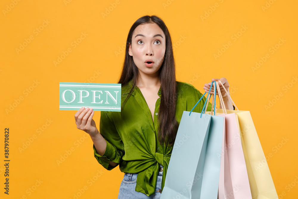 Amazed young brunette asian woman 20s in basic green shirt standing hold package bags with purchases