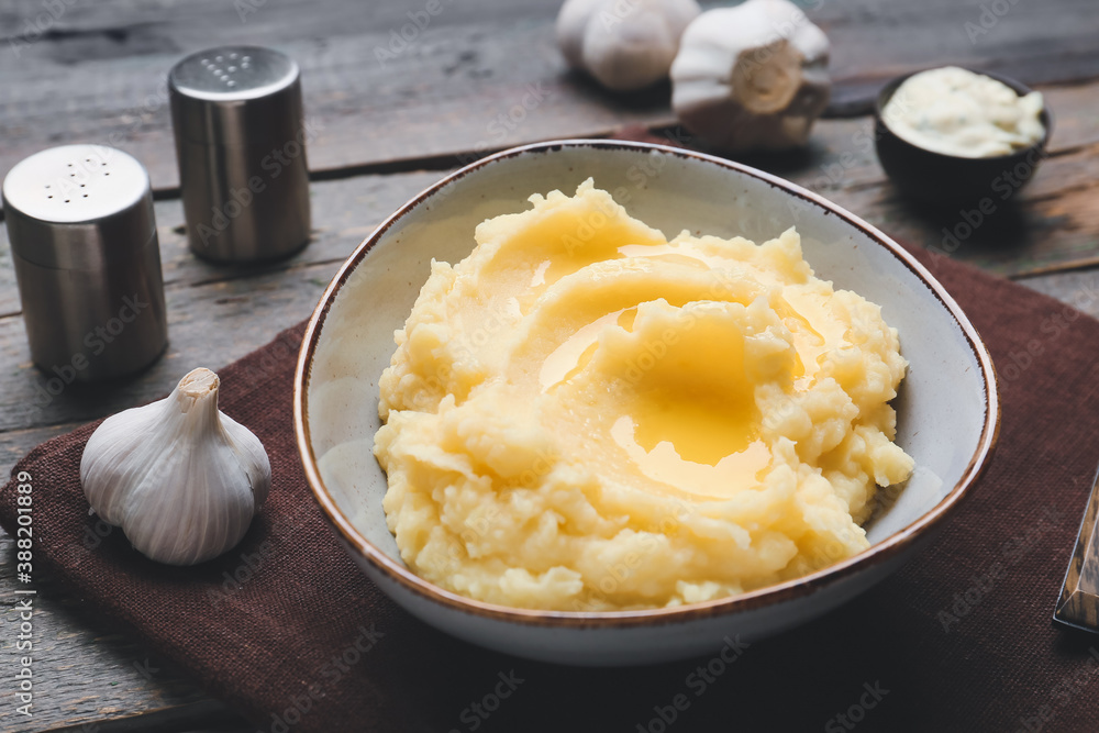 Bowl with tasty mashed potato and garlic on table