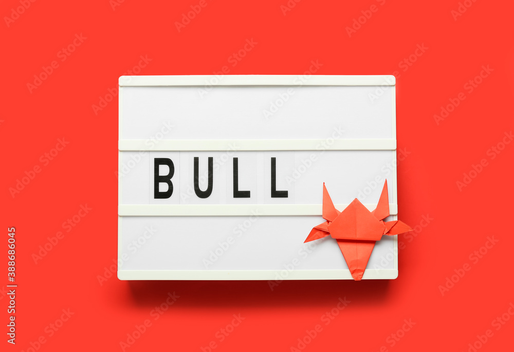 Board with origami bull as symbol of year 2021 on color background