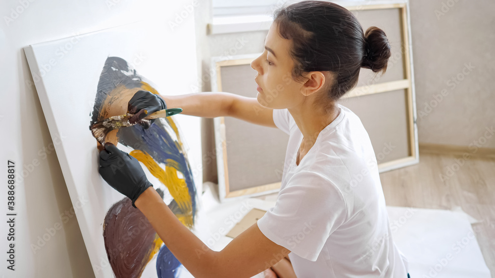 elegant girl artist sits on wooden floor and draws with hands in black gloves and brush at home sunl
