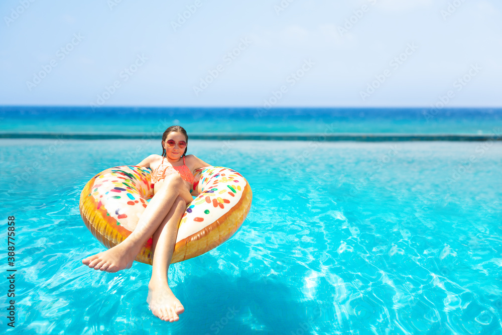 Teenage girl in sunglasses swim on inflatable doughnut in the pool smiling with sea on background