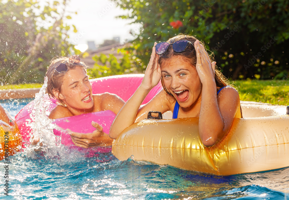 Two teens boy and girl play laughing in swimming pool splashing with inflatable toys