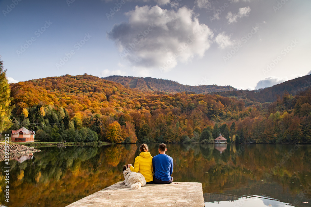 couple and dog sitting by beautiful autumn lake