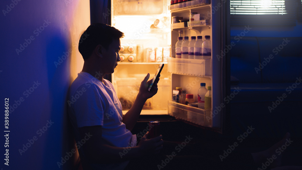 亚洲男人，他正在打开冰箱。晚上喝软饮料，他用了电话。