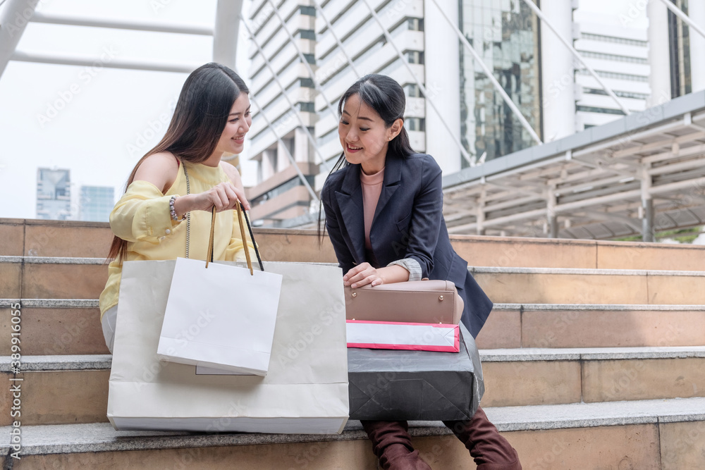 Two young asian woman holding shopping bags and looking on stair