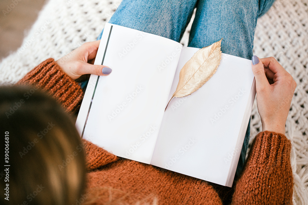 一个女人坐在针织地毯上，打开的笔记本上有一片金色的脆叶子