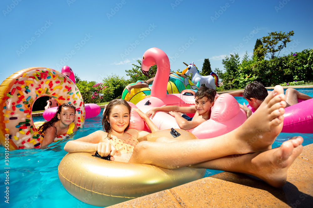 Many friends and smiling girl in group of children play, have fun in swimming pool outside pose with