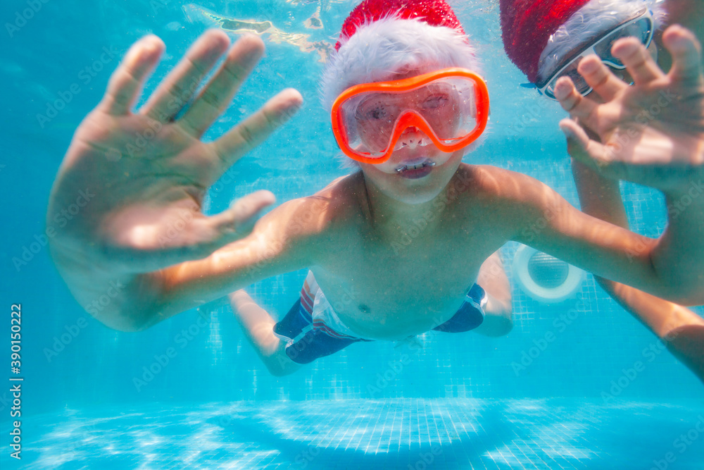 Happy boy pose underwater wearing Santa Claus hat in the pool diving and swimming