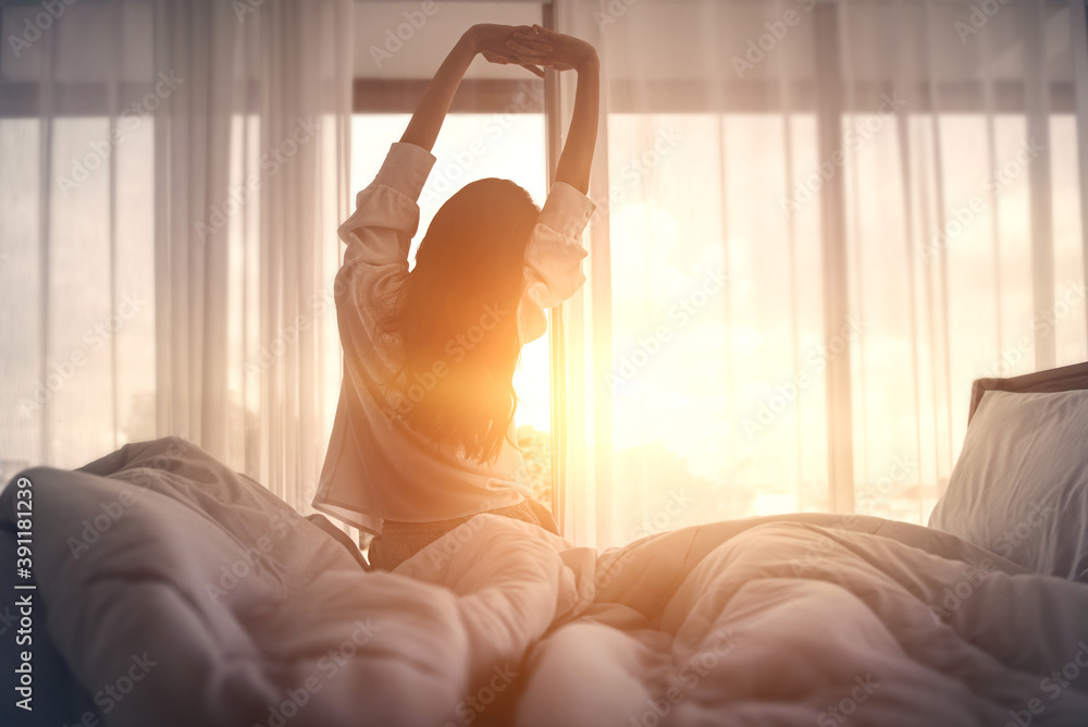 早上醒来后，女人在床上伸着手，新的一天和快乐的周末的概念。