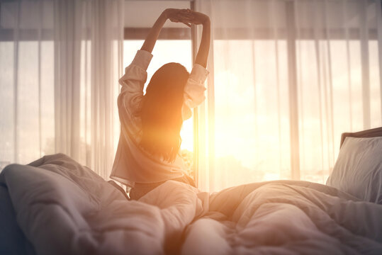 女人早上醒来后在床上伸展双手，新的一天的概念和快乐的周末。