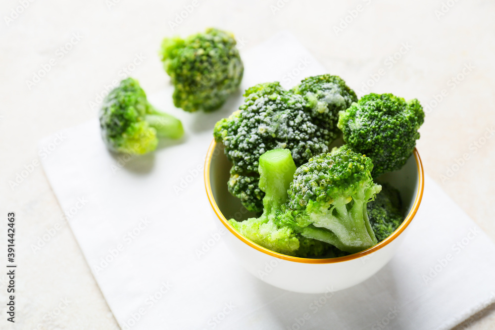 Bowl with frozen broccoli on light background