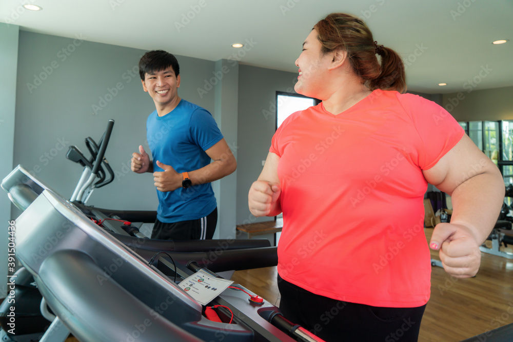 两名亚洲教练男子和一名超重女子在健身房跑步机上锻炼，教练用力拍打