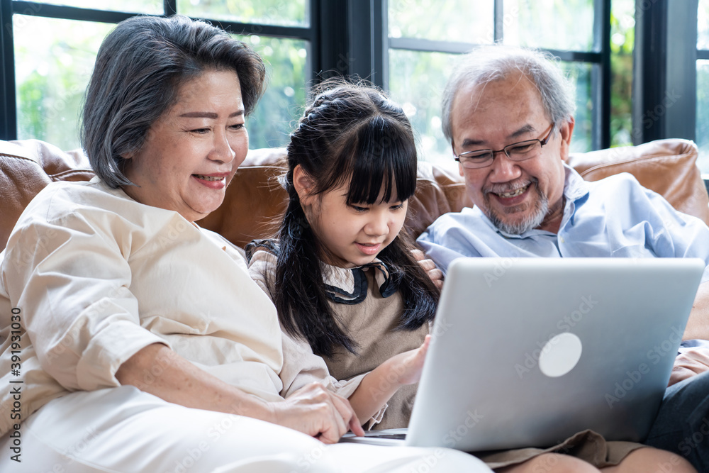 亚洲祖父母看着他们的孙子在用笔记本电脑学习。