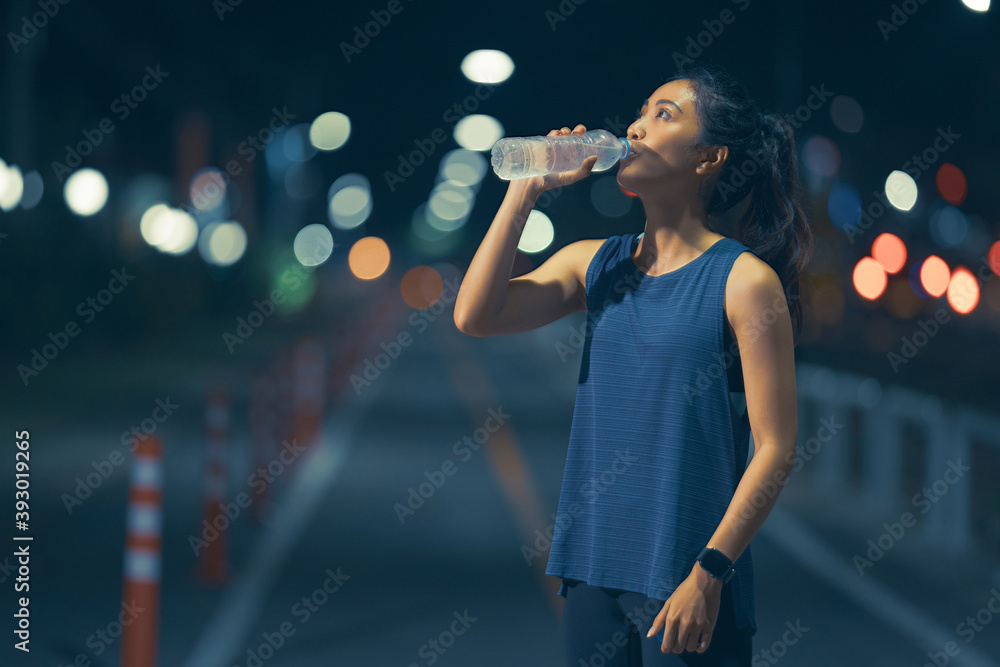 亚洲女性在锻炼和跑步，她在喝水。