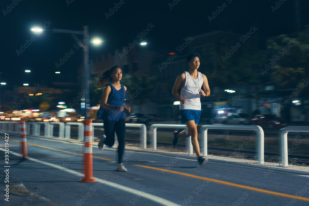 一对亚洲情侣晚上在城市街道上慢跑。
