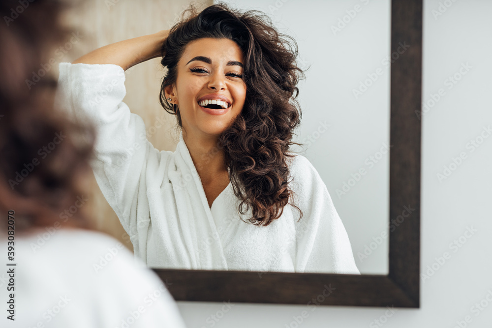 浴室里快乐的女人。年轻的女人在镜子前玩她的头发。