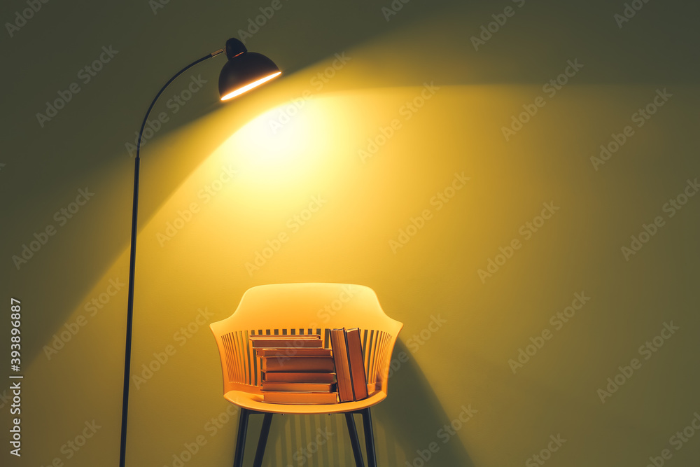 Chair with books and lamp near color wall
