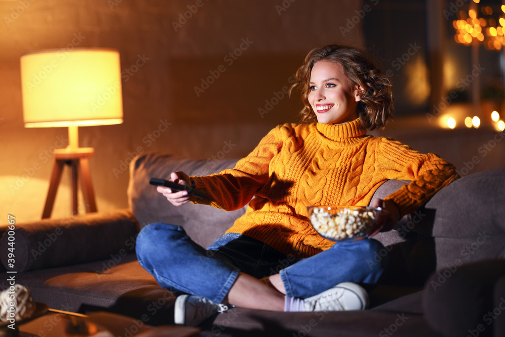 年轻快乐的女人一边吃爆米花，一边在电视上看电影，一边用遥控器切换频道