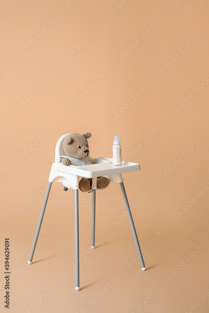 泰迪熊坐在彩色背景的婴儿高脚椅上